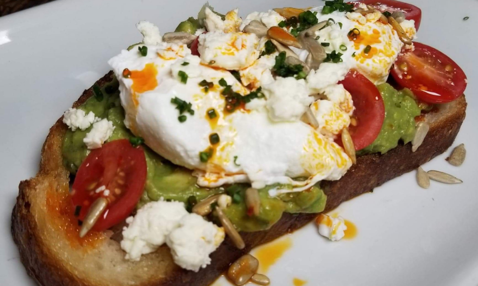 Brunch menu - Avocado Toast - sourdough toast, avocado, feta cheese, cherry tomatoes, aleppo oil, sunflower seeds, two poached eggs. Photo by Nick Rama