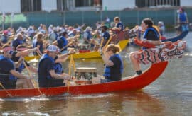 Colorful dragon boat race with team paddling on water, vibrant outdoor event, energetic competition, community celebration.