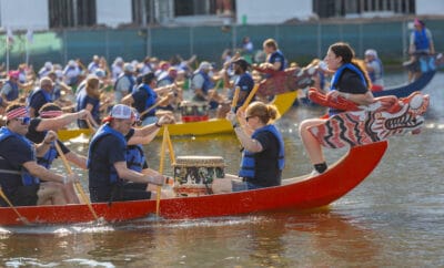 Colorful dragon boat race with team paddling on water, vibrant outdoor event, energetic competition, community celebration.