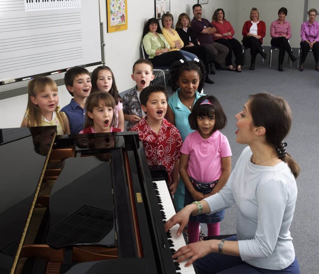 YMES_Class_singing_at_piano-2048×1763